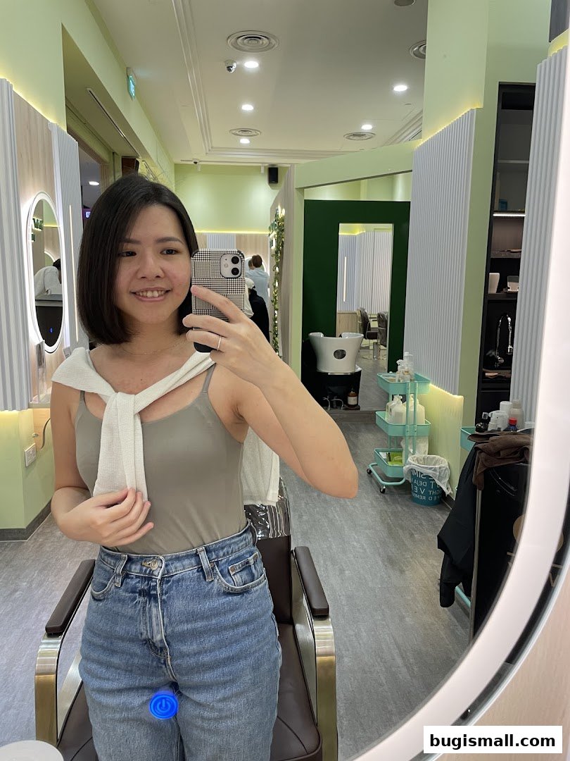 A woman smiles at the camera in a brightly lit salon, reflecting in a large mirror.