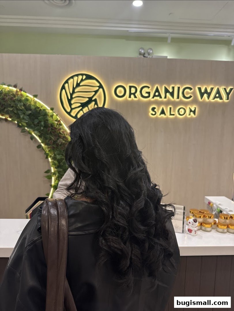 A person with curly hair stands in front of the Organic Way Salon reception desk.