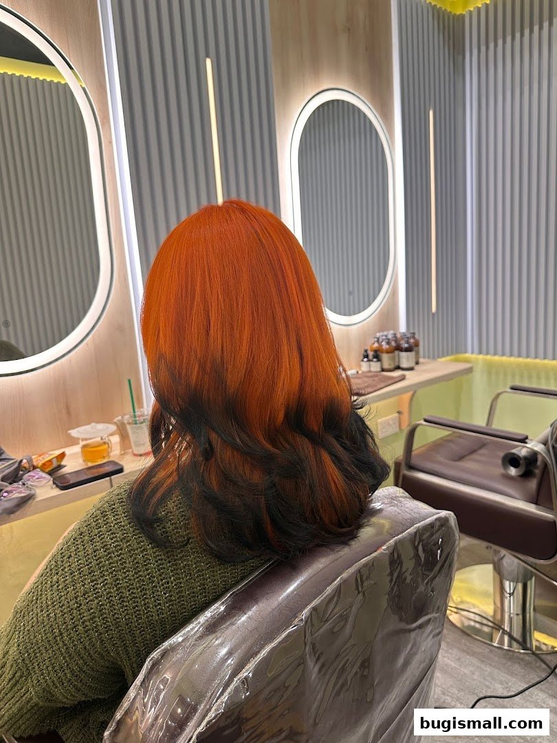 A person with vibrant orange and black ombre hair sits in a salon chair, facing away from the camera.