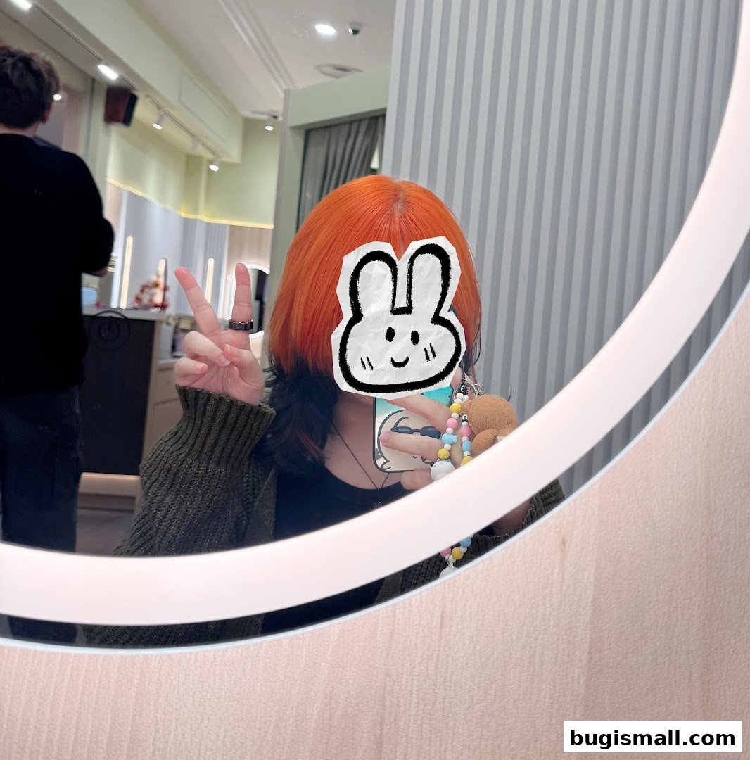 A person with bright orange hair poses in a salon mirror, showing off their new hairstyle.
