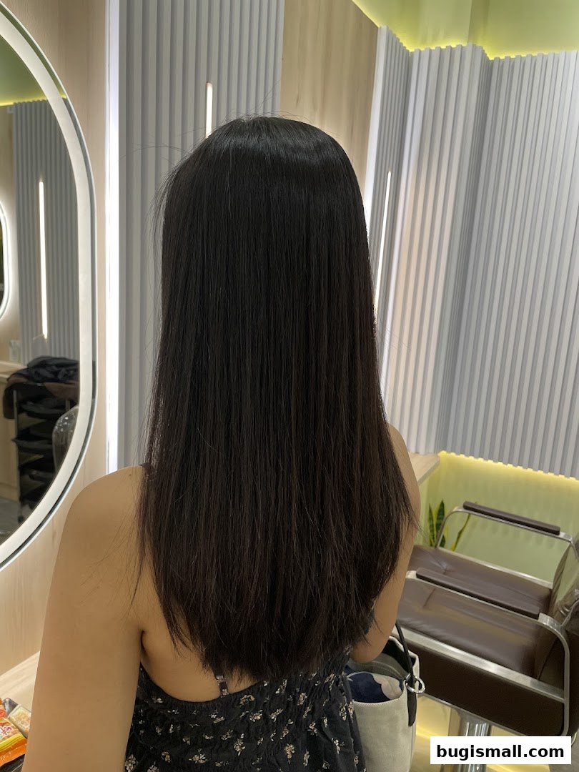 A person with long, dark, straight hair is shown from behind in a salon.