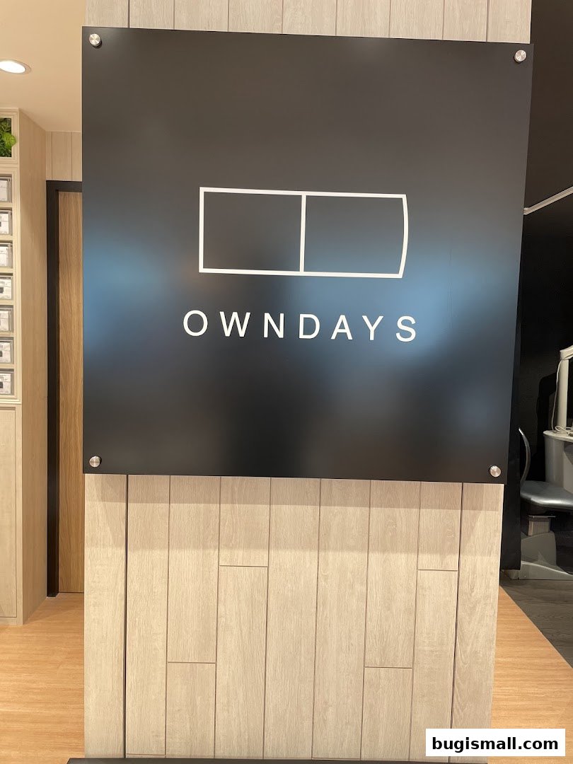 A sign with the OWNDAYS logo and name is displayed on a wooden panel wall.
