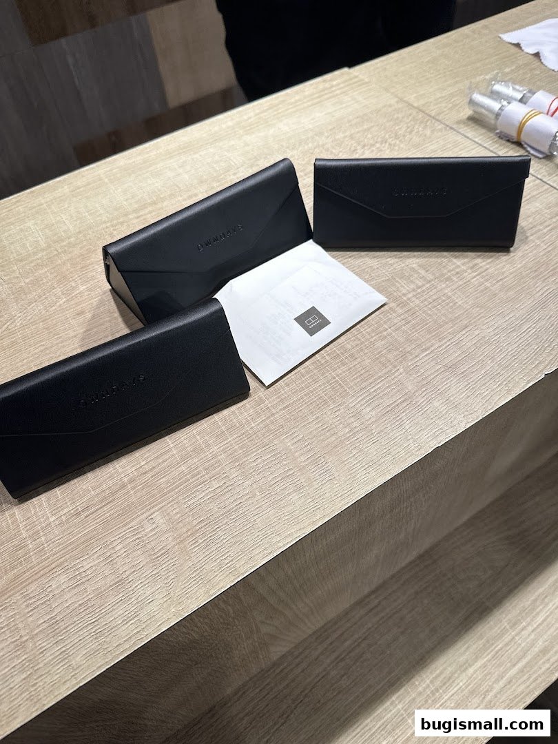 Three black OWNDAYS glasses cases and a white paper with the OWNDAYS logo on a wooden counter.