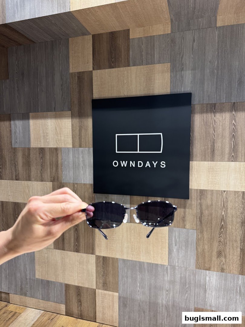 A hand holds up stylish sunglasses in front of the OWNDAYS logo.