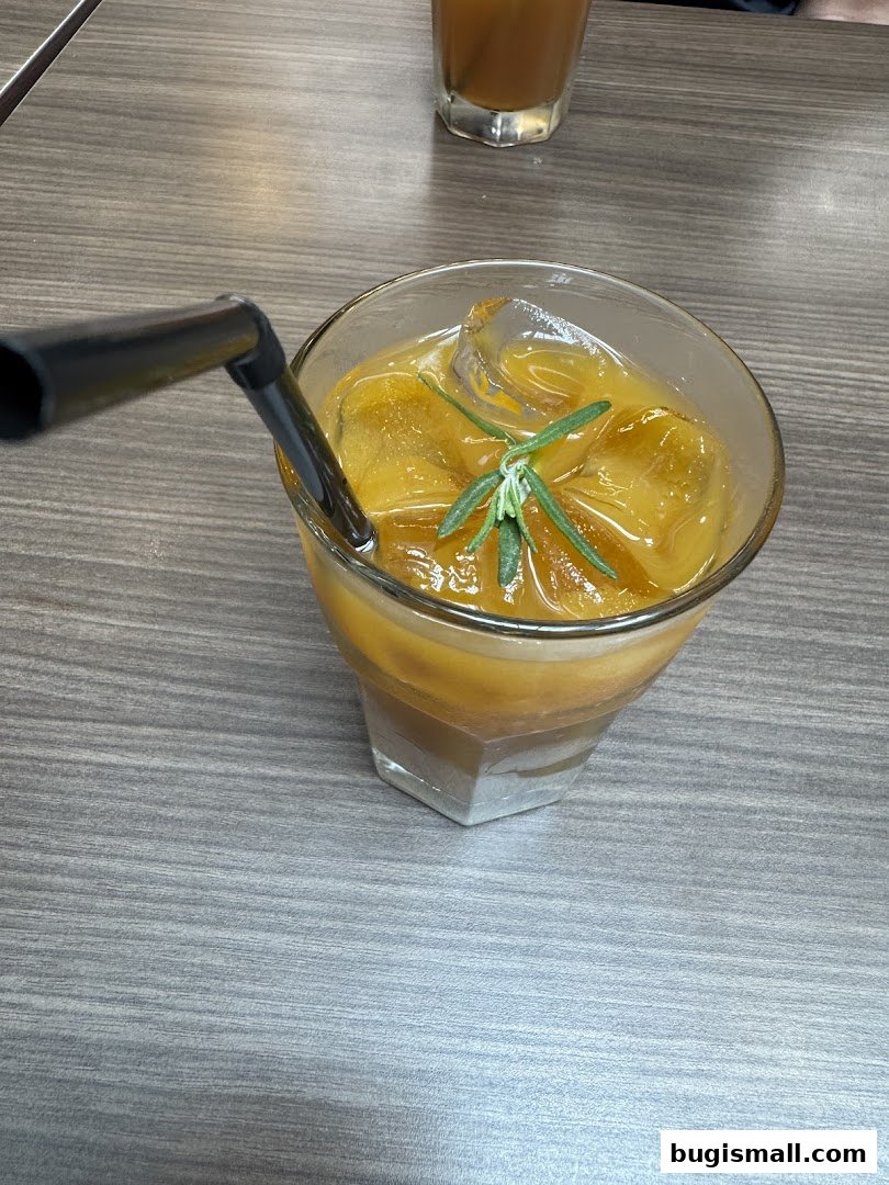 A refreshing iced beverage with orange juice, ice, and a sprig of rosemary.