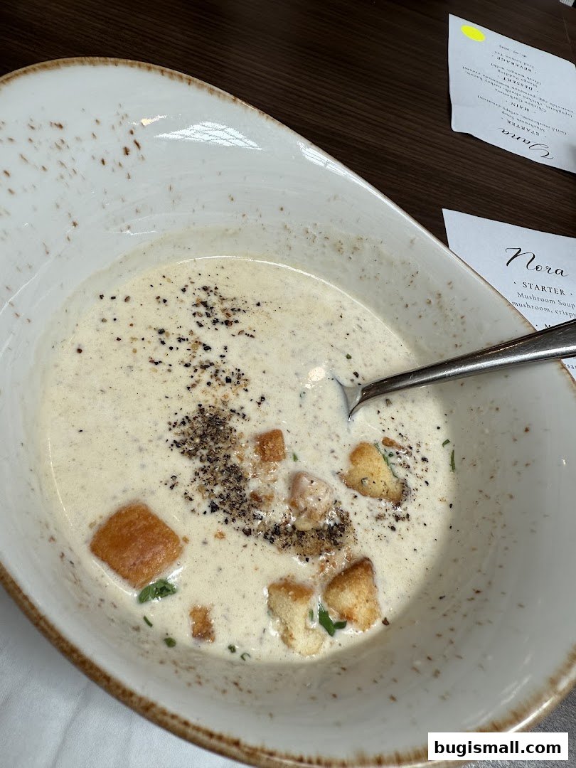A bowl of creamy mushroom soup with croutons and herbs, served with a menu.