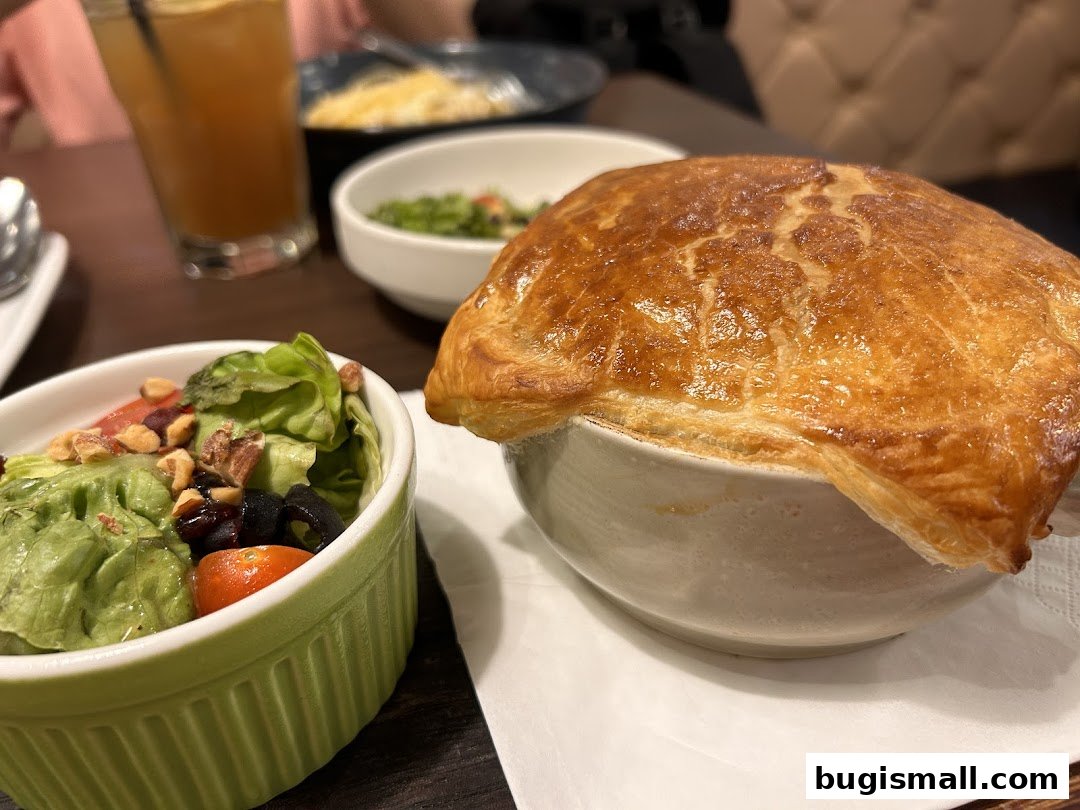 A close-up of a golden-brown pastry-topped dish with a side salad and a drink.