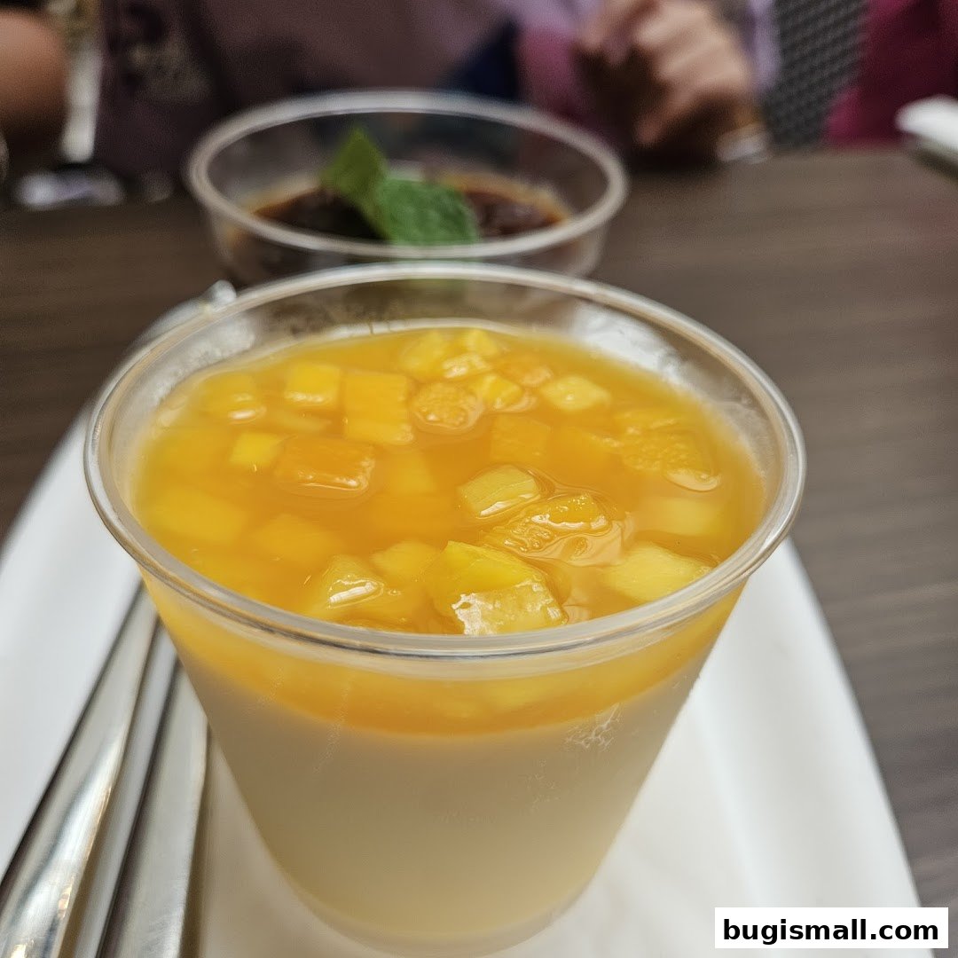 A close-up of a dessert with mango chunks in a clear cup, with another dessert in the background.