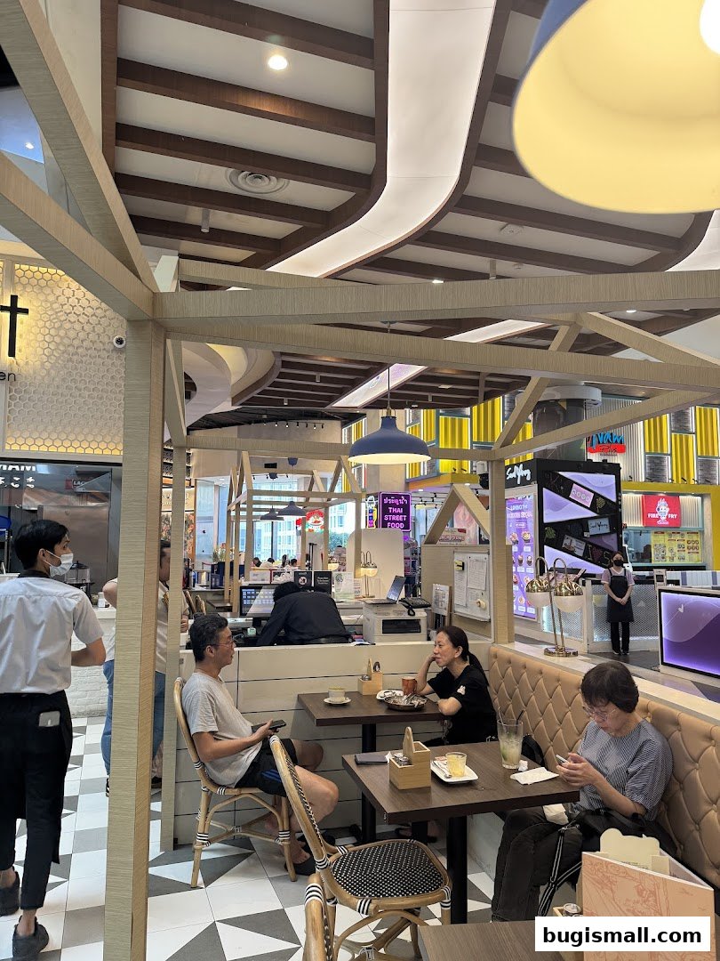 Diners enjoy meals at tables inside a modern restaurant with a unique wooden beam ceiling.