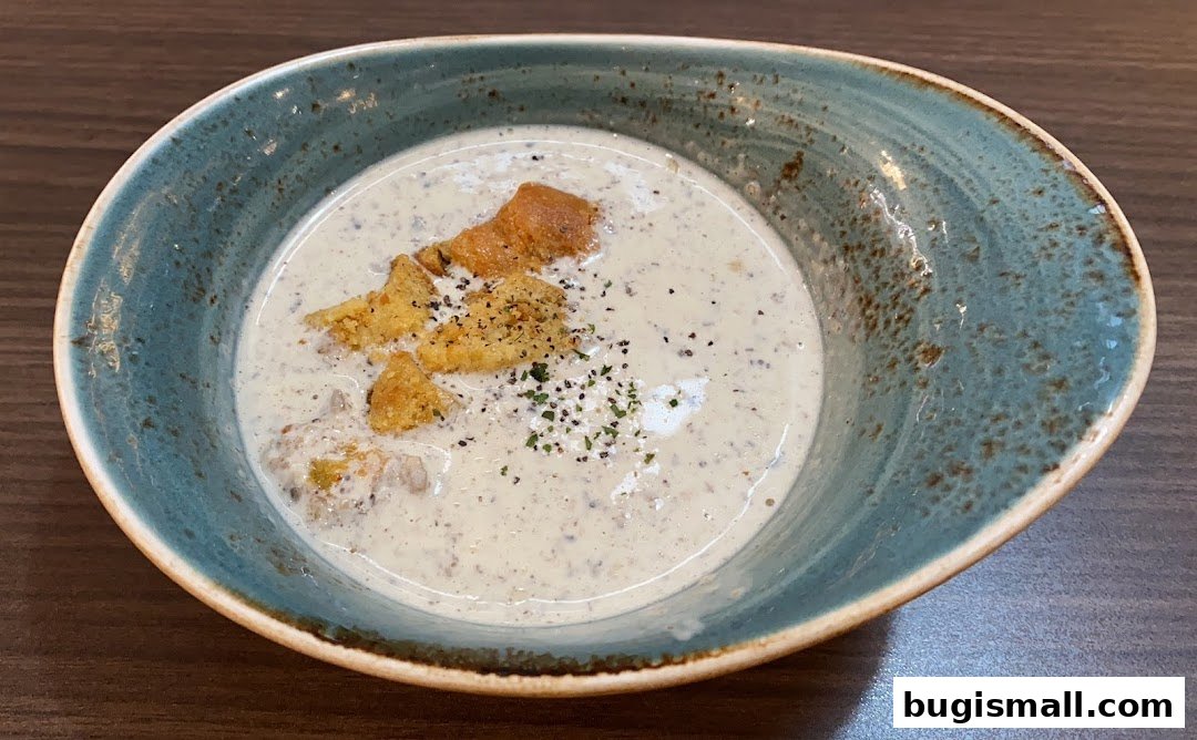 A close-up shot of a creamy mushroom soup with croutons and herbs in a rustic bowl.