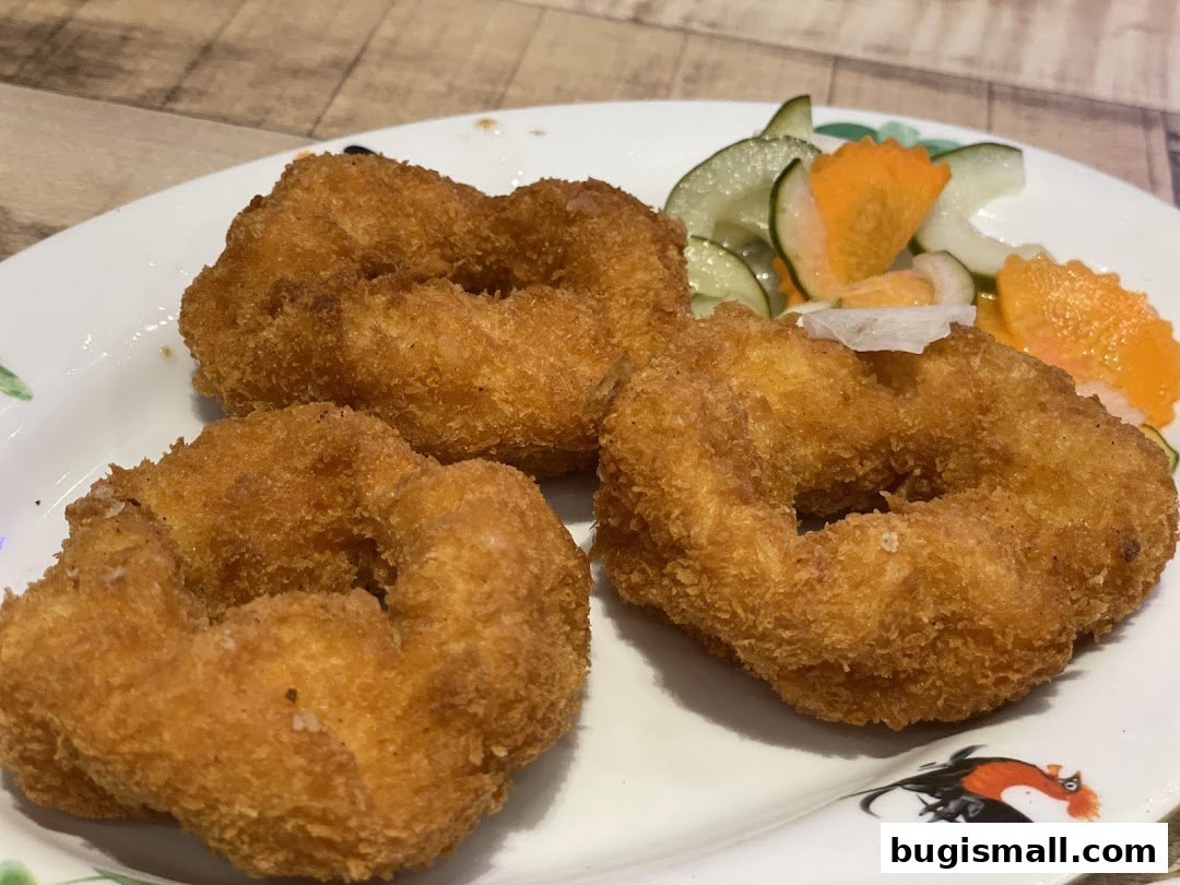 Three golden-brown, crispy fried shrimp rings served with a side of sliced cucumbers and carrots.