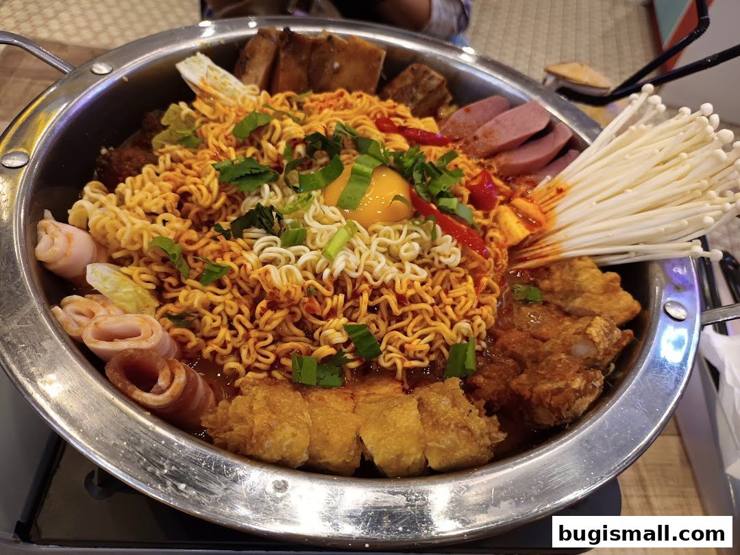A steaming pot of Korean army stew with noodles, meat, vegetables, and an egg.