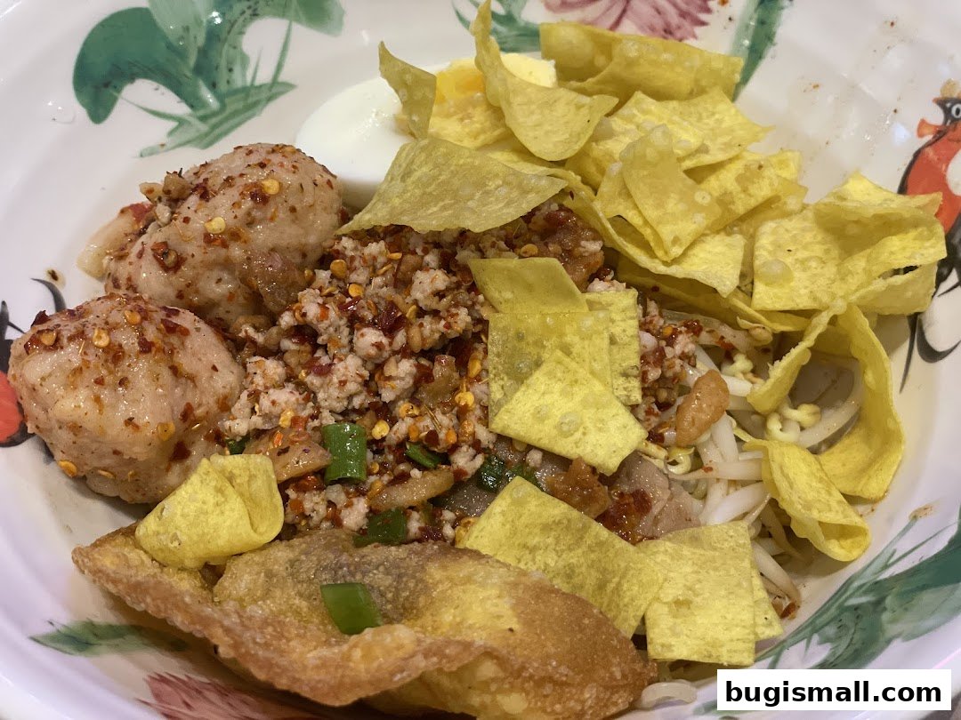 A close-up of a delicious bowl of Thai noodles with meatballs, minced meat, and crispy wonton chips.