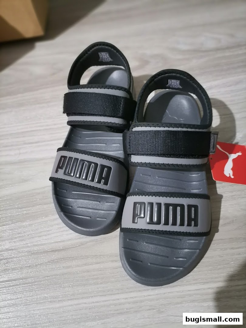 A pair of grey Puma sandals with black straps and the Puma logo.
