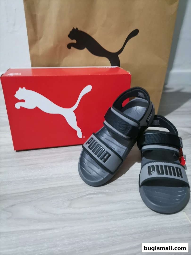 A pair of grey Puma sandals with a red Puma shoebox and shopping bag.