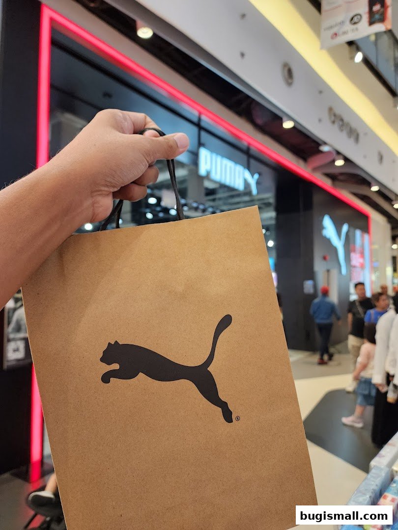 A hand holds a Puma shopping bag in front of the Puma store.