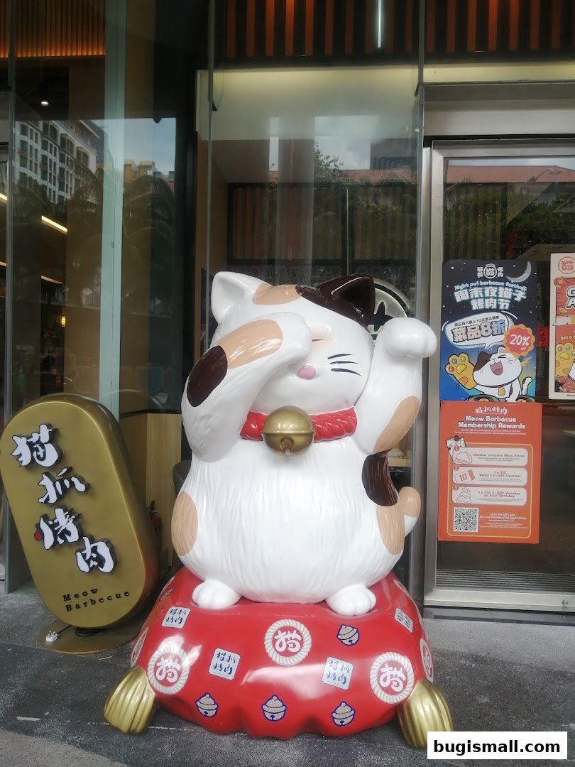 A large Maneki-neko statue sits outside a shop with Chinese and English signage.