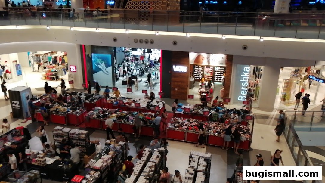 Busy shopping mall interior with various clothing stores and sale displays.