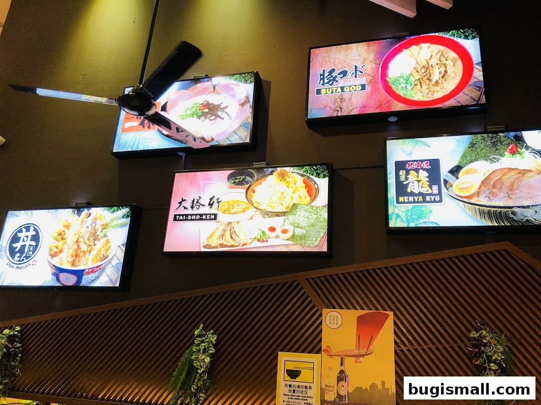 Illuminated displays of various ramen dishes and tempura are mounted on a dark wall.