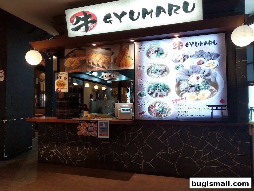 A ramen shop counter with a large illuminated menu displaying various ramen dishes.