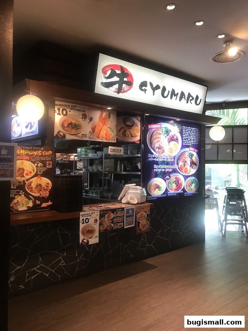 A ramen shop counter with menu displays and a prominent Gyumaru sign.