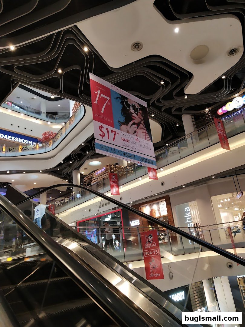 A shopping mall interior with escalators and various shop fronts, featuring a promotional banner.