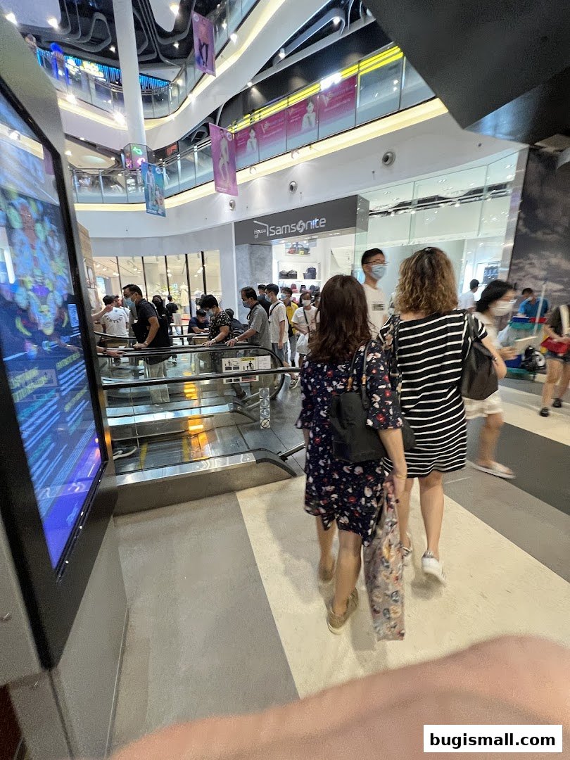 People walking past a Samsonite store entrance in a mall with escalators.