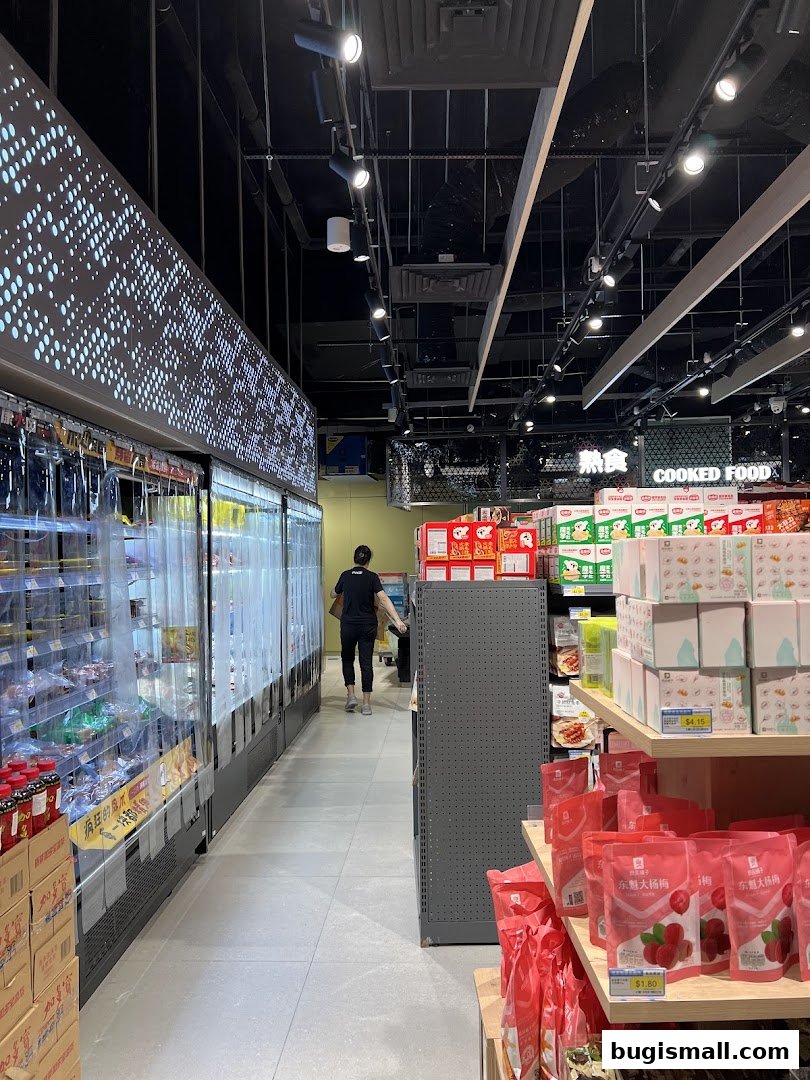 A person walks down the aisle of a brightly lit supermarket with refrigerated displays and shelves of products.