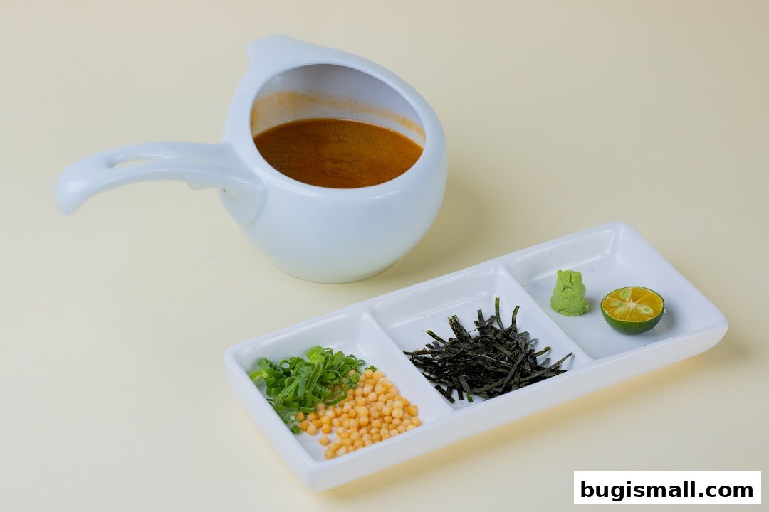 A white pitcher of broth with a side dish of chopped scallions, crispy rice, seaweed, wasabi, and lime.