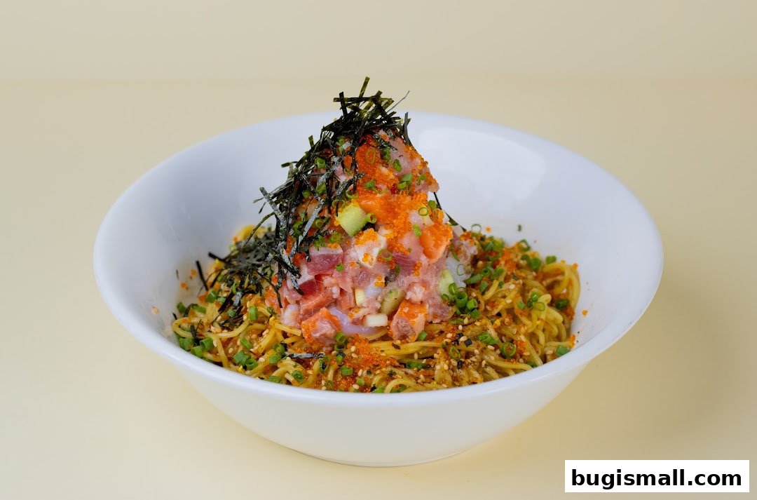 A bowl of noodles topped with fresh tuna, salmon, tobiko, and seaweed.