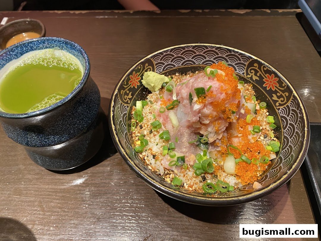 A bowl of scrambled egg rice with toppings and a cup of green tea.