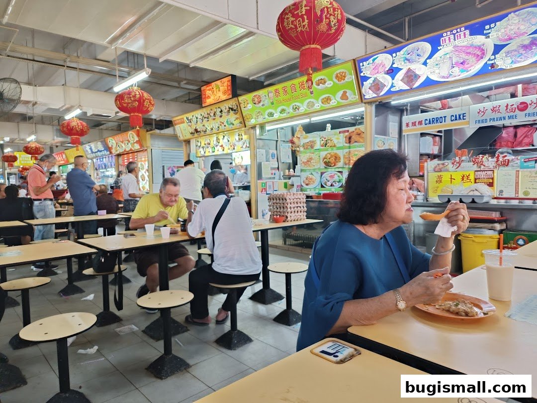 People eating at a food court with various food stalls and menus displayed.