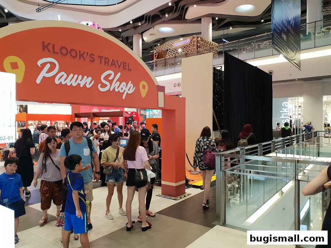 A busy mall concourse with a Klook's Travel Pawn Shop event and shoppers.