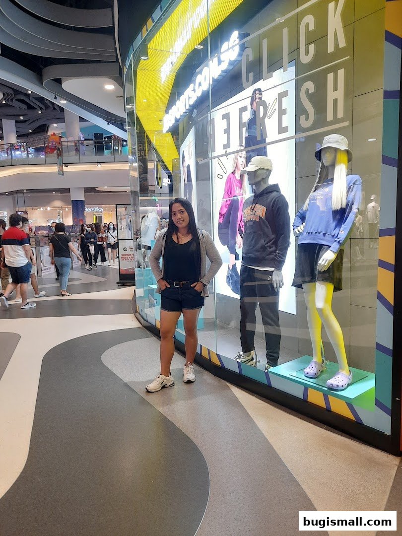 A woman stands in front of a shop window displaying mannequins and fashion.