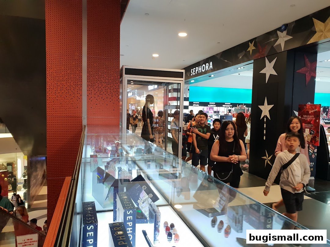 People are seen queuing outside a Sephora store with displays of beauty products inside.