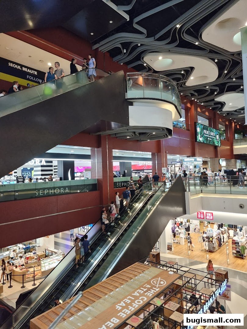 People on escalators in a busy shopping mall with Sephora and Uniqlo stores visible.