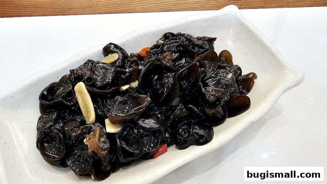A close-up of a white dish filled with glistening black wood ear mushrooms and garlic.