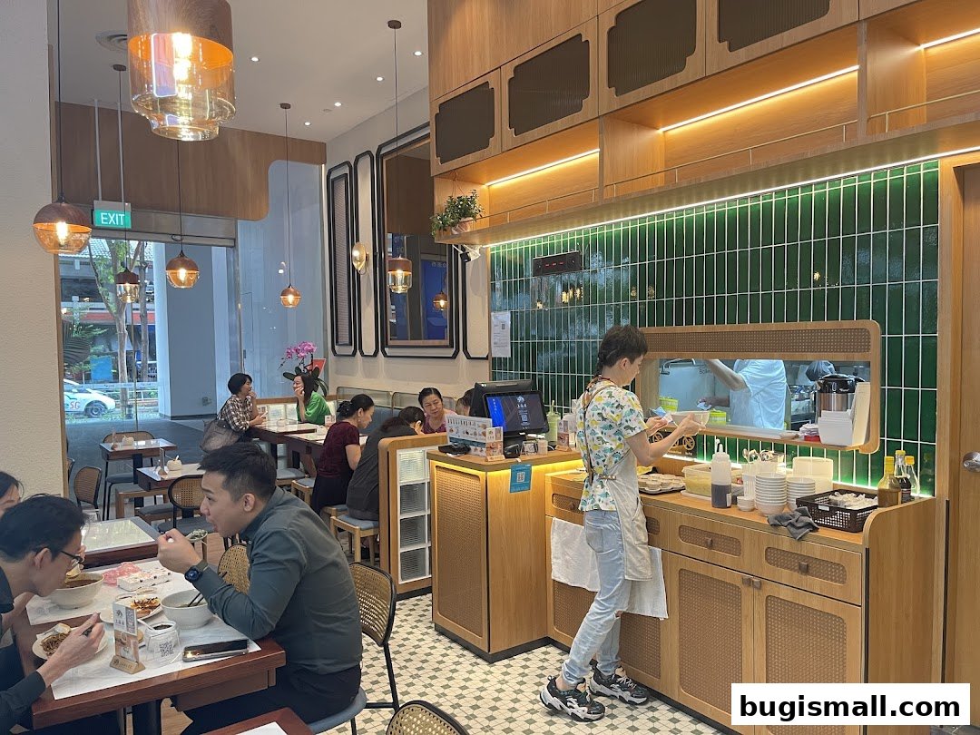 Interior of a modern restaurant with diners and staff preparing food behind a counter.