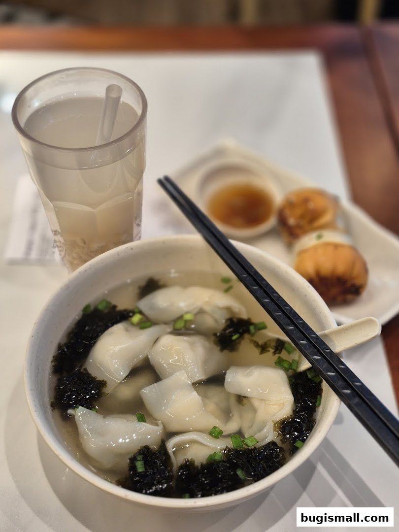A bowl of wonton soup with pan-fried buns and a drink.
