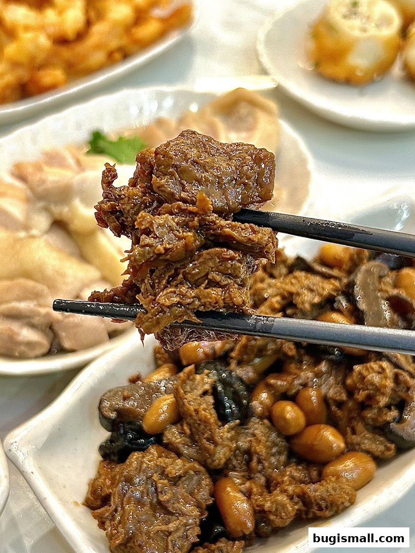 Chopsticks holding a piece of braised meat with peanuts and mushrooms.