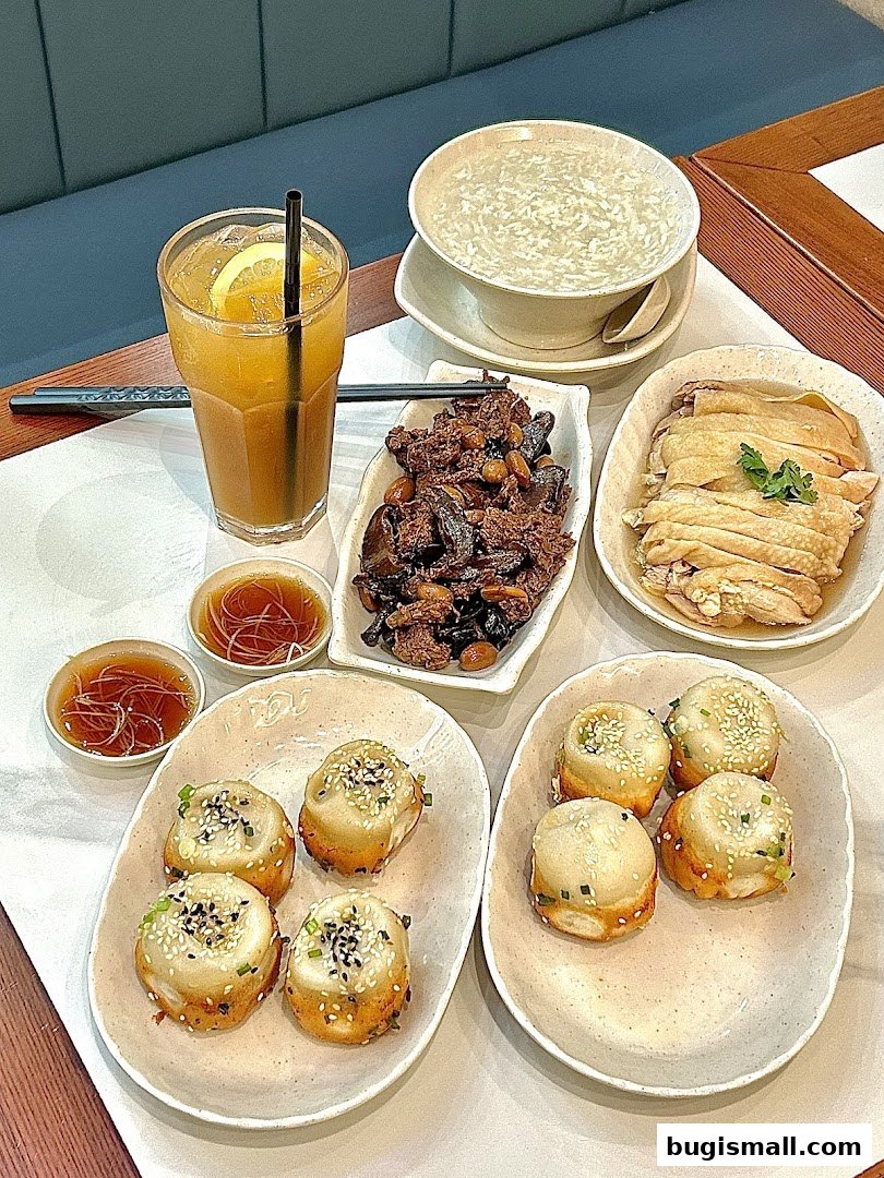 A table filled with delicious Shanghai Tan pan-fried buns, chicken, soup, and a refreshing drink.