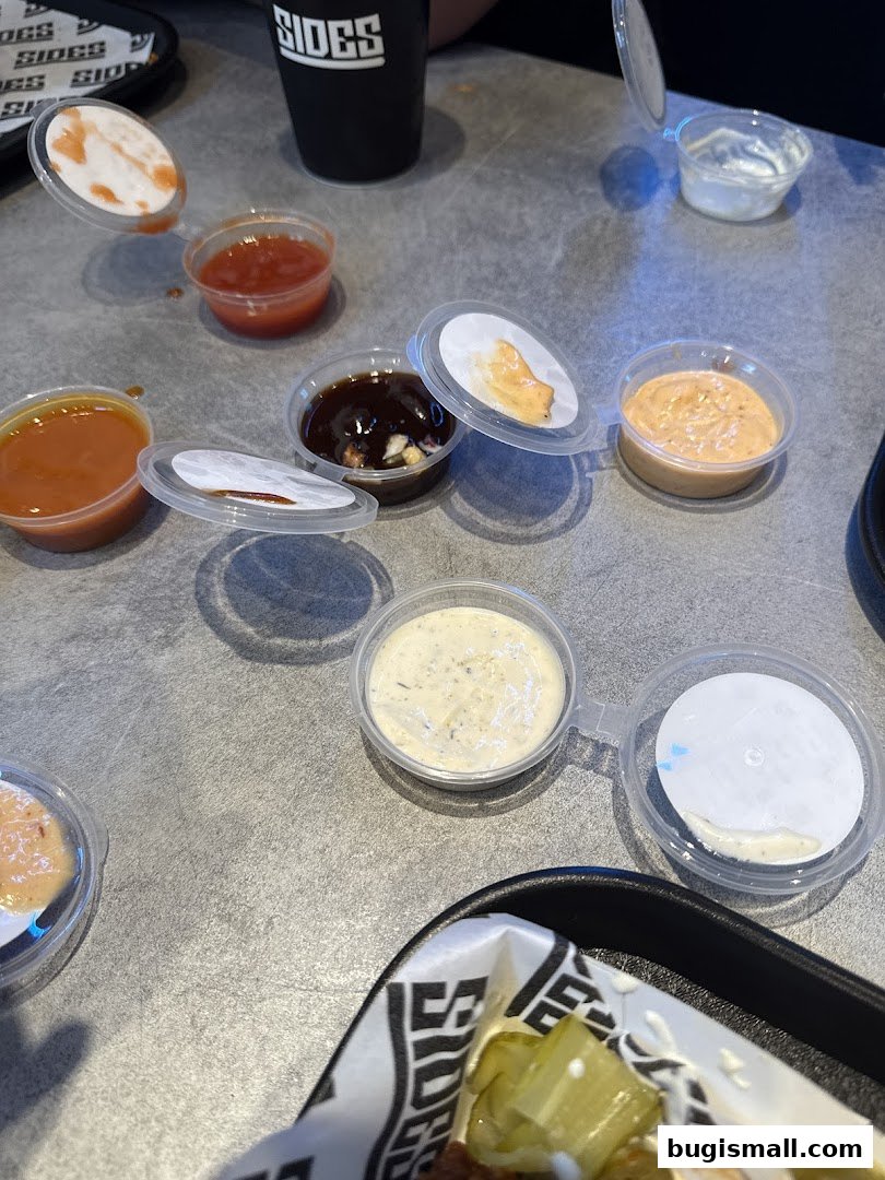A variety of dipping sauces are arranged on a table next to a cup with the shop's logo.