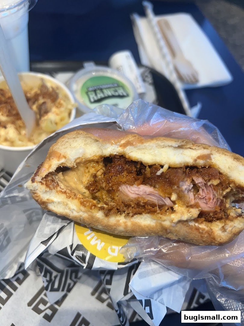 A close-up of a loaded sandwich with a side of mac and cheese and a ranch dip.