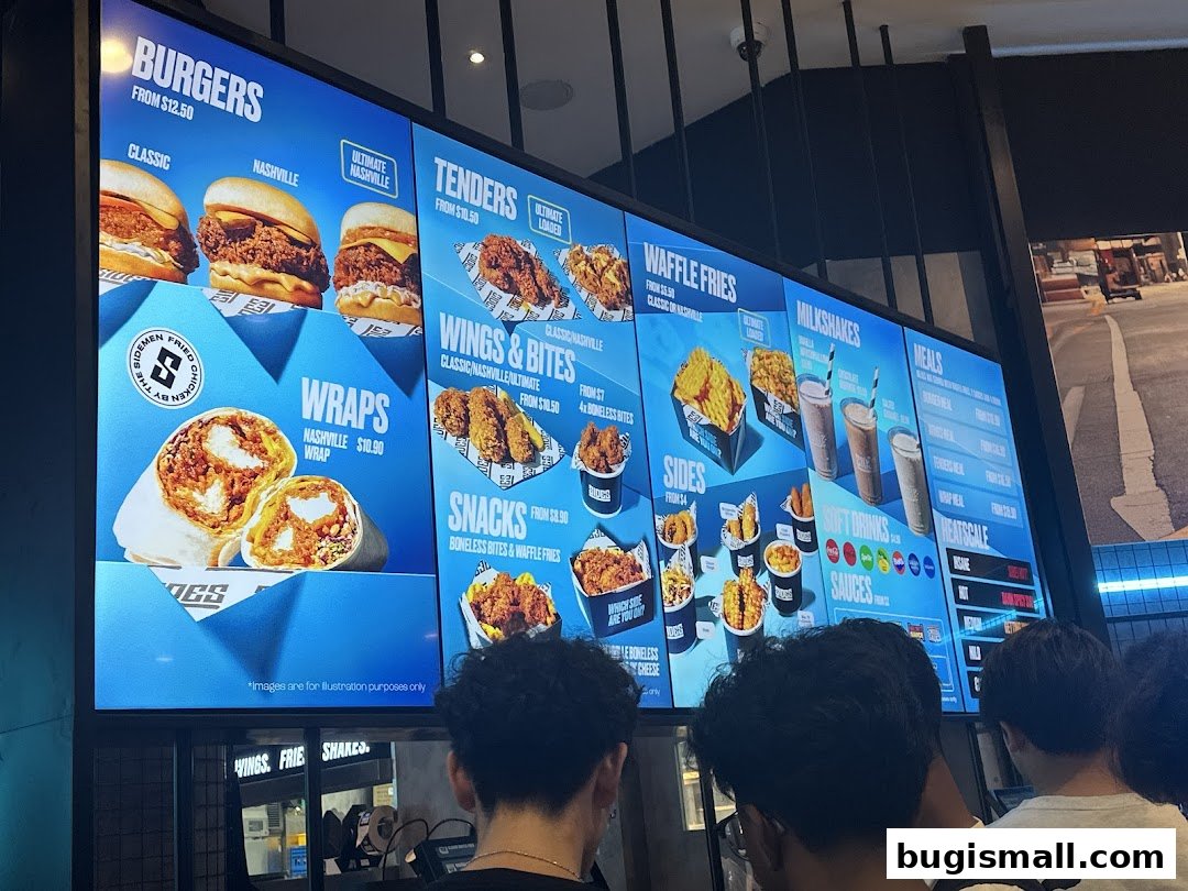 A digital menu board displaying various burgers, wraps, tenders, wings, sides, milkshakes, and meals.