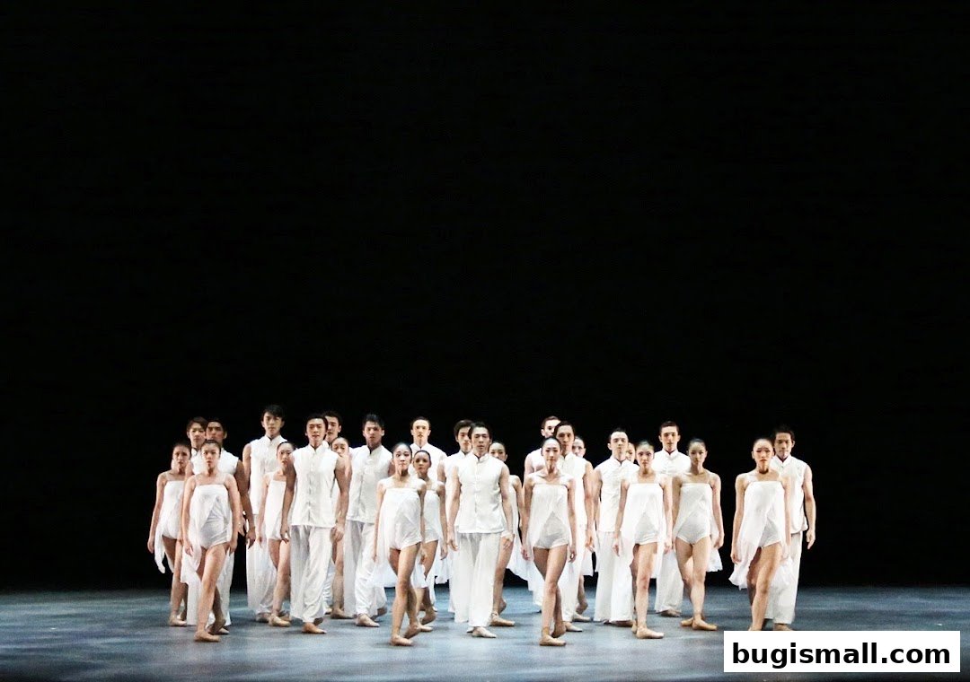 A group of dancers in white costumes stand on a stage with a black background.