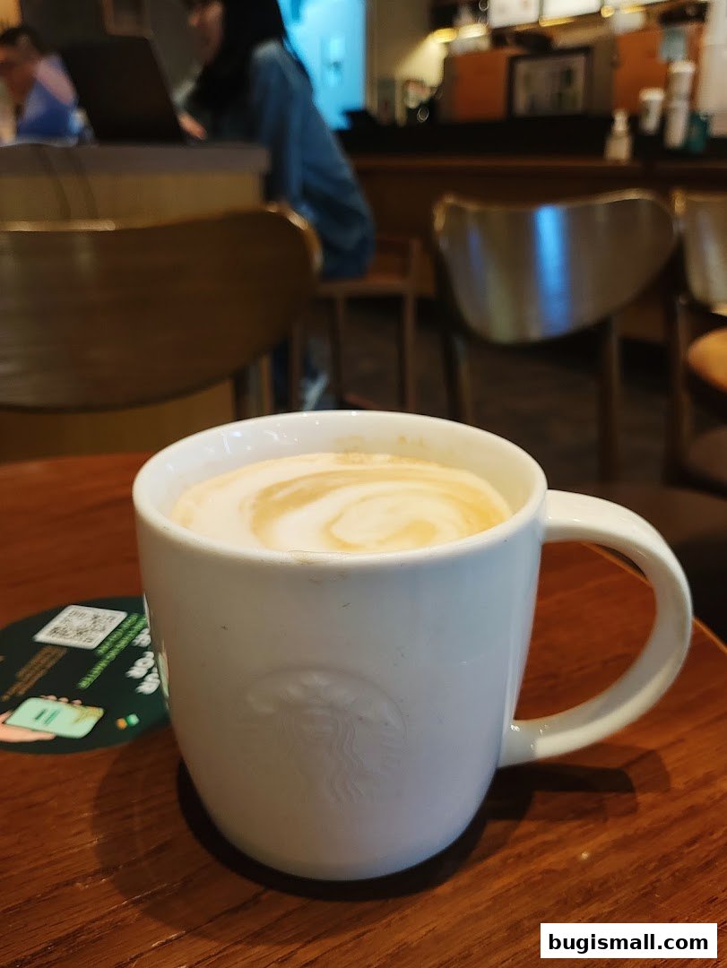 A close-up of a white Starbucks mug filled with a latte on a wooden table.