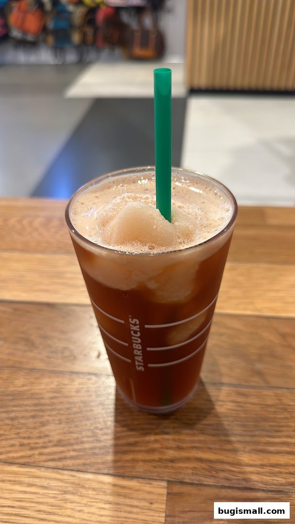 A close-up of a Starbucks iced beverage with a green straw on a wooden surface.
