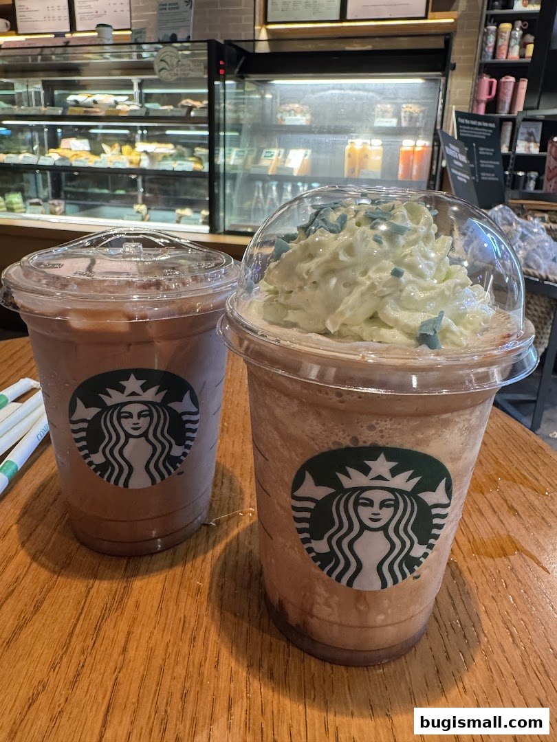 Two Starbucks drinks with whipped cream and sprinkles on a wooden table.
