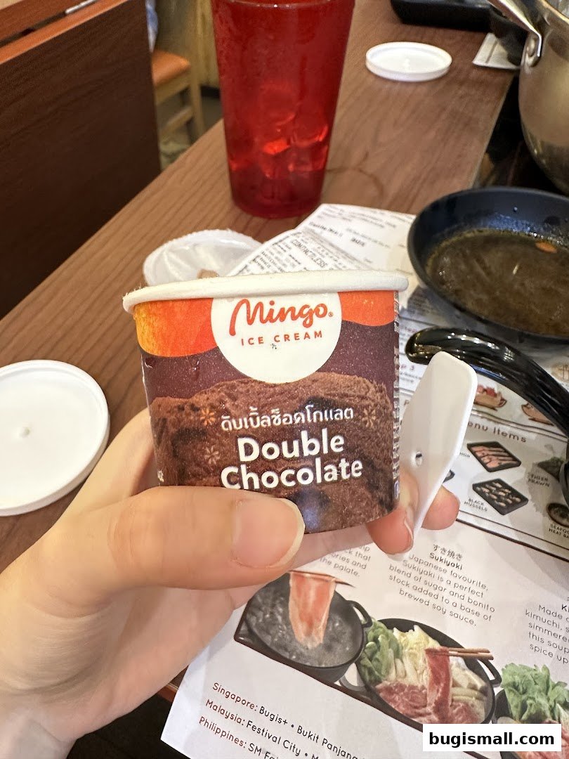 A person holds a cup of Mingo Double Chocolate ice cream with a shabu shabu menu in the background.