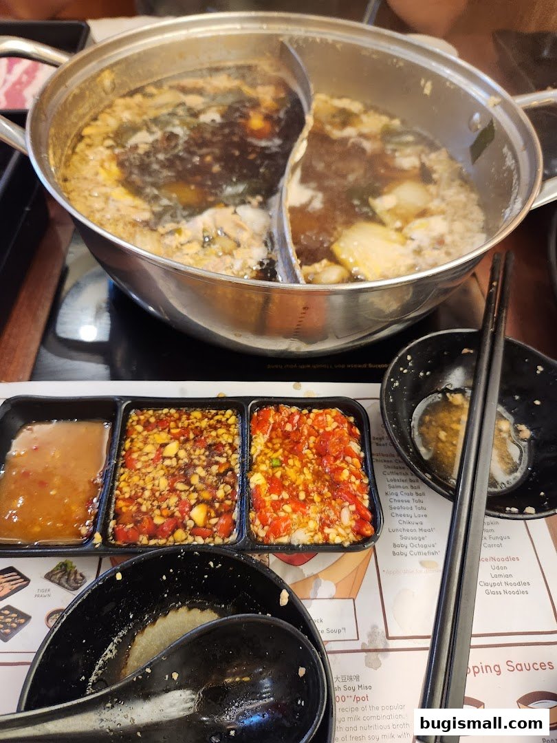 A split pot of shabu-shabu broth with dipping sauces and chopsticks.